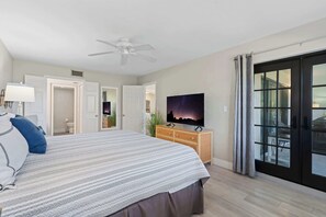 Un dormitorio con cama, televisión, ventilador de techo y puerta corrediza de vidrio al exterior.