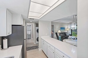 Une cuisine moderne équipée d’un lave-linge et d’un sèche-linge intégrés, un coin repas avec une table et des chaises, et une vue sur l’extérieur.