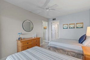 Un dormitorio con dos camas, ventilador de techo, cómoda, espejo y decoración en las paredes.
