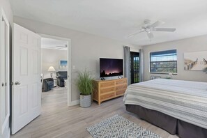 A bedroom with a bed, a TV, a ceiling fan, a window with blinds, and a door leading to another room. - F-338 -Beautiful Resort and Sunset Views! (Naples)