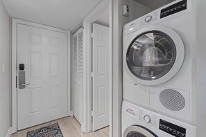 Una sala de bugaderia amb una rentadora i assecadora Bosch, una porta blanca i una catifa amb dibuixos.