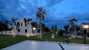A flat roof with a white surface and a black edge, surrounded by trees and houses with lights.