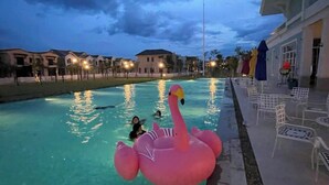 A swimming pool with a pink flamingo float, surrounded by lounge chairs and a building with a white facade.