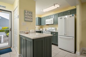 A kitchen with green cabinets, a white refrigerator, a microwave, and a stove.