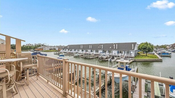 Ein Ufergrundstück mit Anlegesteg, ein Gebäude mit Zugang zum Steg und eine Holzterrasse mit Außenbestuhlung.