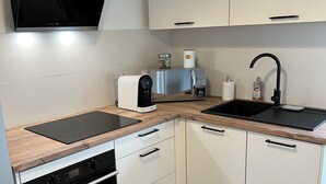 A compact kitchen with a built-in oven, a microwave, a coffee maker, a sink, and a flat-screen TV mounted above the counter.