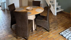 A dining area with a round wooden table, wicker chairs, and a hanging light fixture.