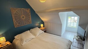 A bedroom with a bed, bedside lamps, a ceiling light, a TV, and a window.