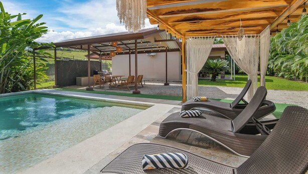 A poolside area with lounge chairs, a covered patio, and a view of the pool. - Casa Heliconias La Fortuna (La Fortuna)