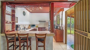 A kitchen with a central island, bar stools, a hanging light fixture, and a view of the outdoors. - Casa Heliconias La Fortuna (La Fortuna)