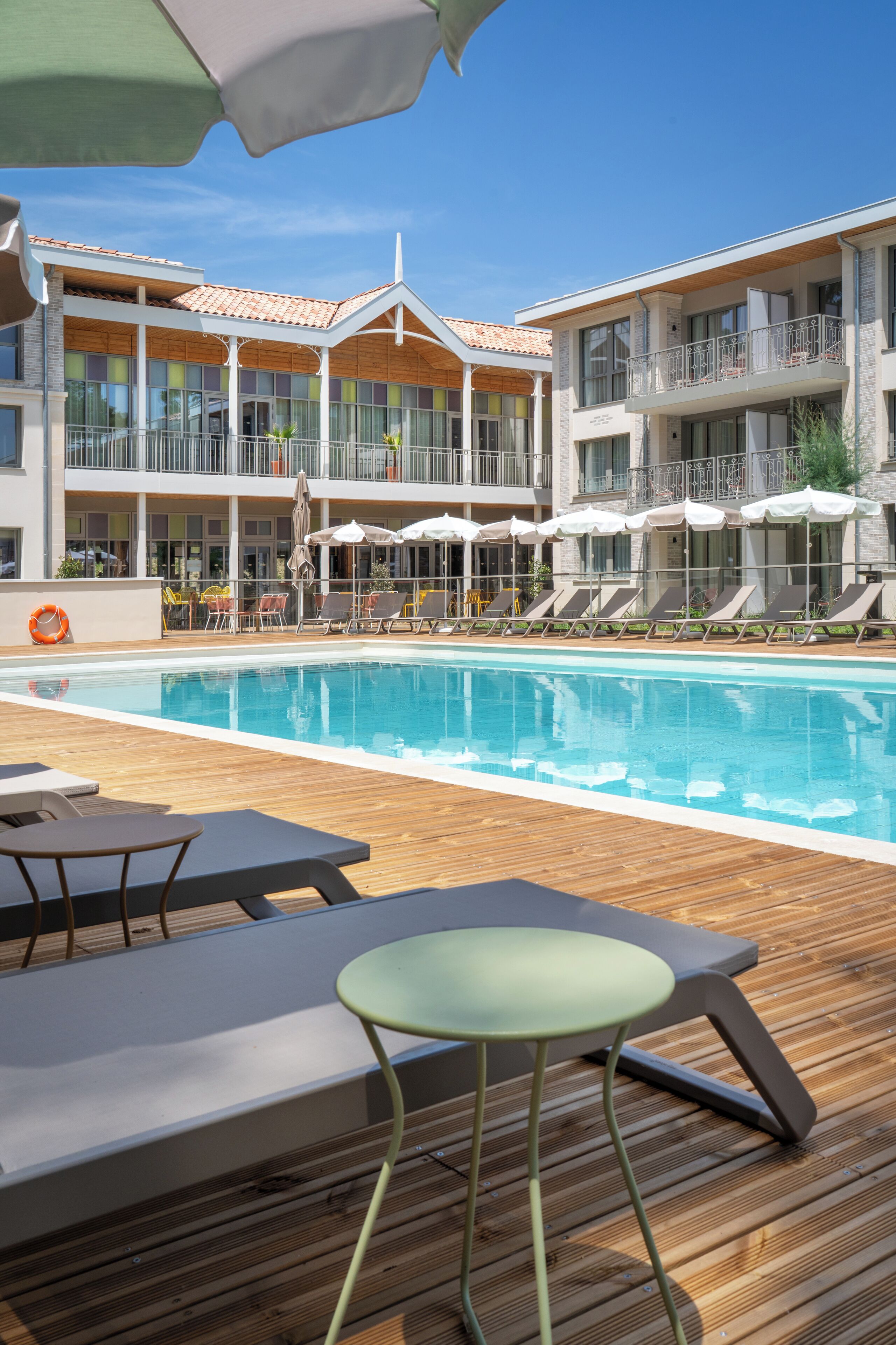 Un área de piscina con sillas de descanso, sombrillas y una terraza de madera.