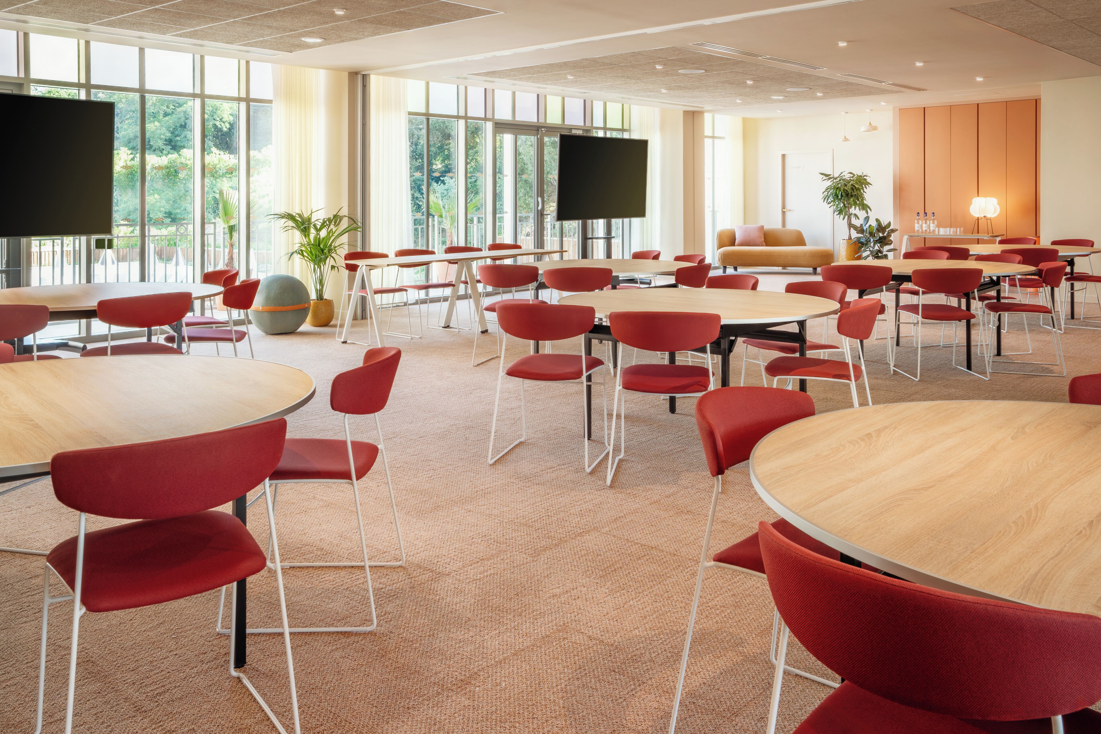 A conference room with multiple tables and red chairs, large windows, and a flat-screen TV.