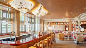 A modern bar area with a wooden counter, bar stools, and a large decorative light fixture.