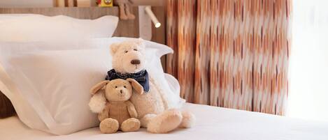 A neatly made bed with two teddy bears, a wooden toy set, and a curtain.
