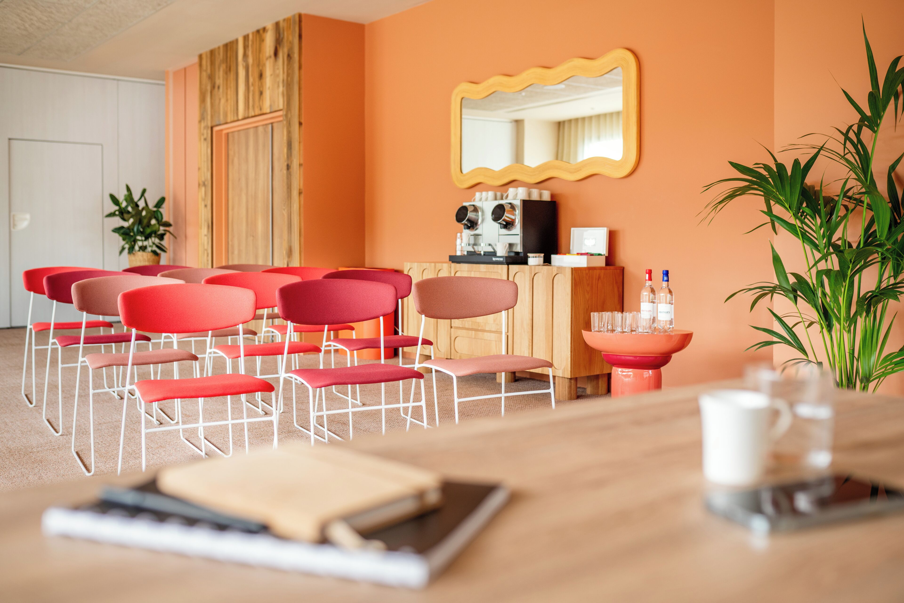 A room with red chairs arranged in a semi-circle, a wooden cabinet with a mirror, and a potted plant.