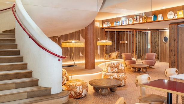 A modern interior with a curved staircase, wooden flooring, and a seating area with round tables and chairs.