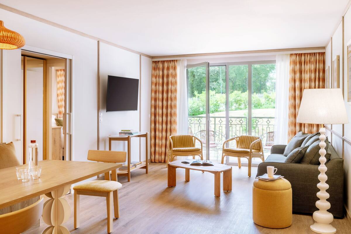 Ein modernes Wohnzimmer mit einem Holzesstisch, zwei Sesseln, einer Couch und einem an der Wand befestigten Fernseher.