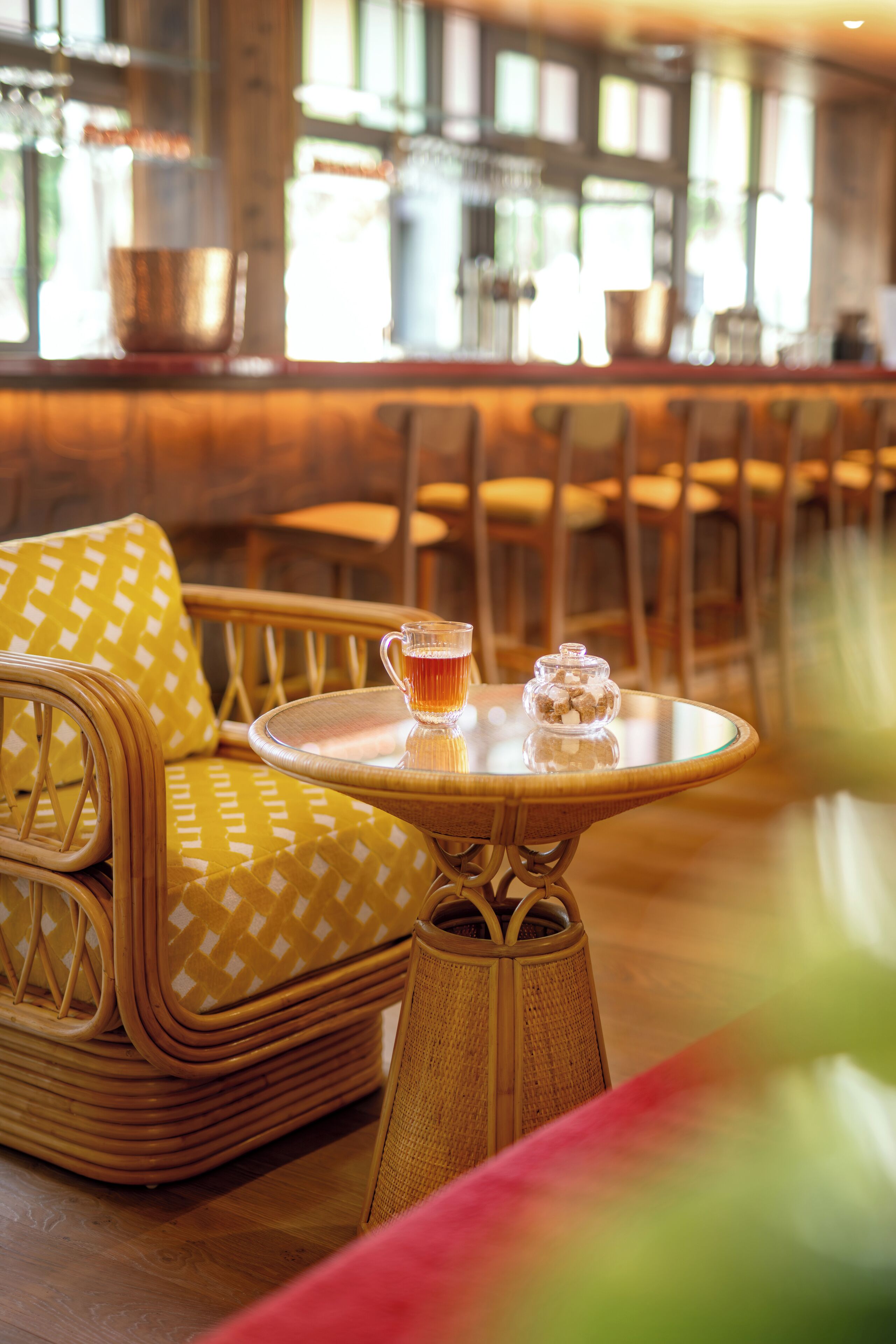 A wicker sofa with yellow cushions and a round table with a glass pitcher and a jar.