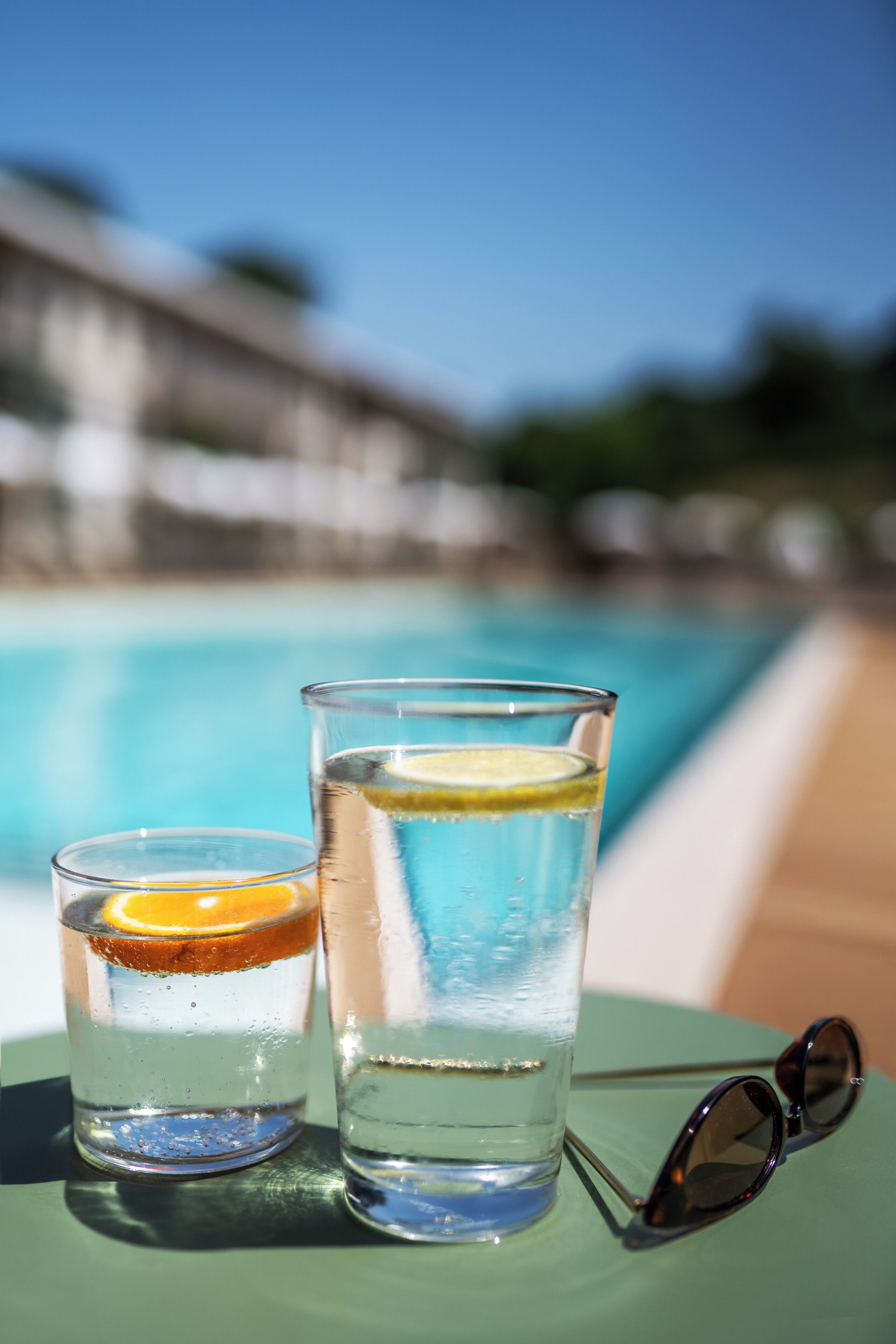 Deux verres d’eau avec des rondelles de citron, posés sur une table au bord d’une piscine.