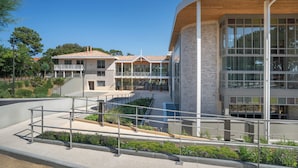 A modern building with a curved facade, large windows, and a covered outdoor area with plants.