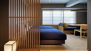 Una habitación de hotel moderna con un ventanal grande, una cama, un escritorio y una separador con listones verticales.
