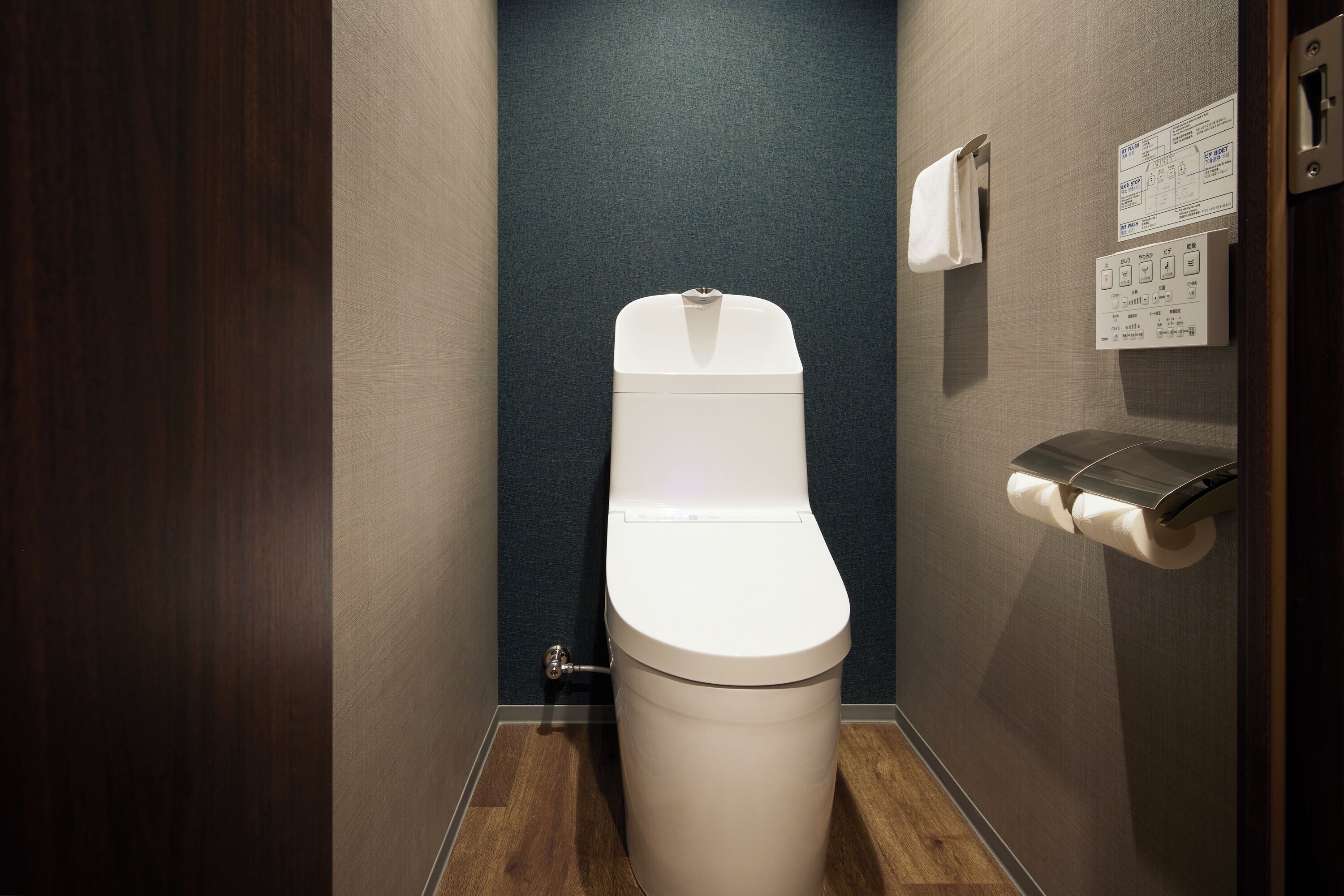 A modern bathroom with a white toilet, a wooden floor, and a dark blue wall.