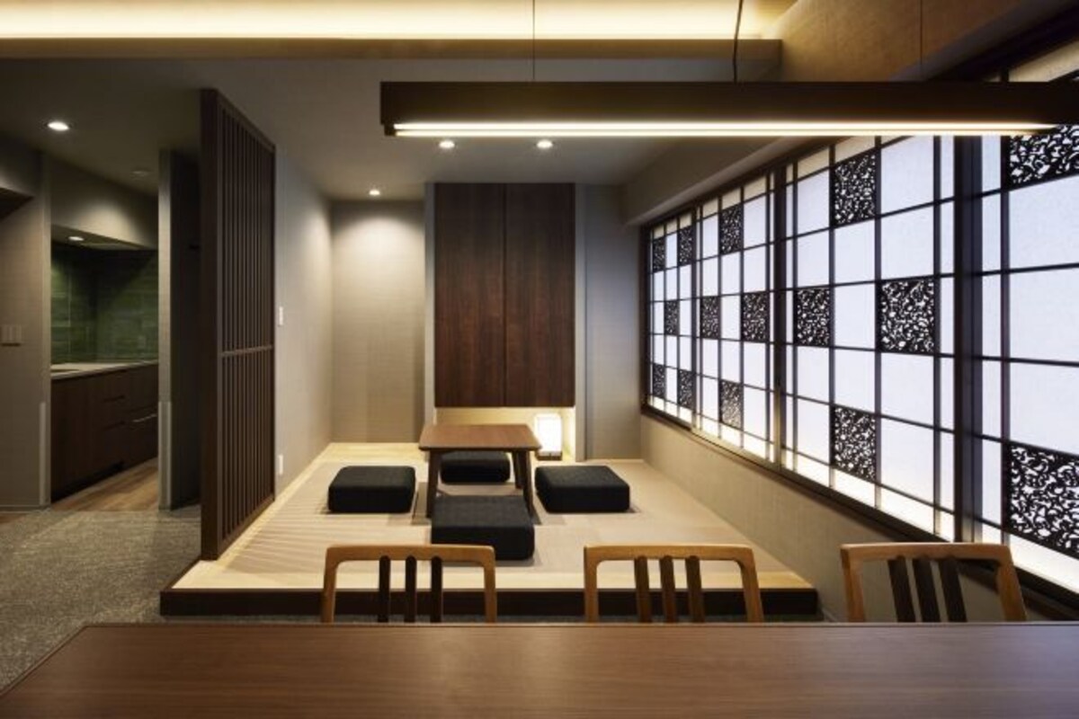 Una habitación moderna con una mesa de comedor de madera, cojines negros y un ventanal con un panel decorativo.
