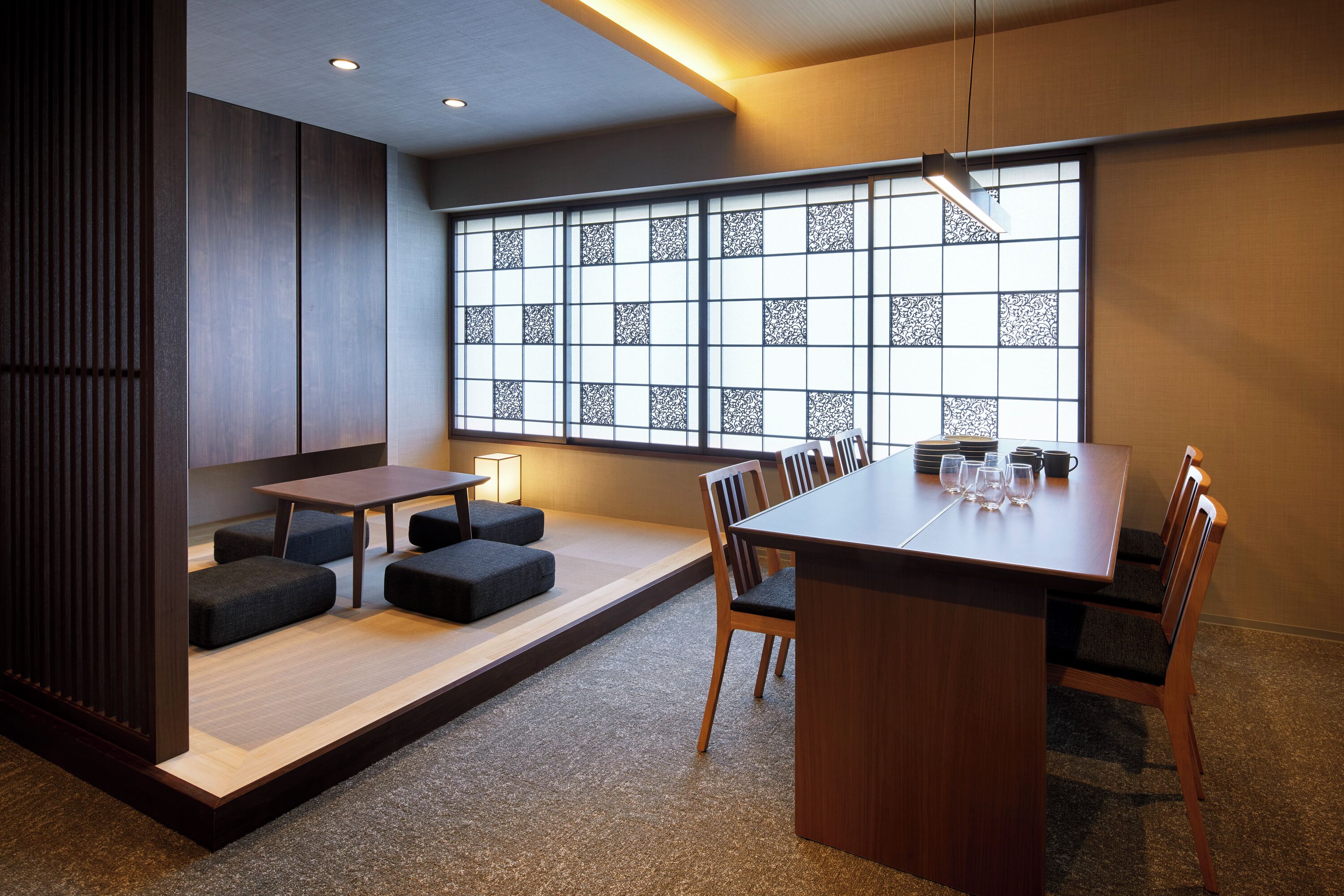 A modern dining area with a wooden table, cushioned seating, and a large window with decorative patterns.