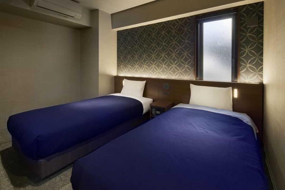 A hotel room with two beds, a window, and a patterned wall.