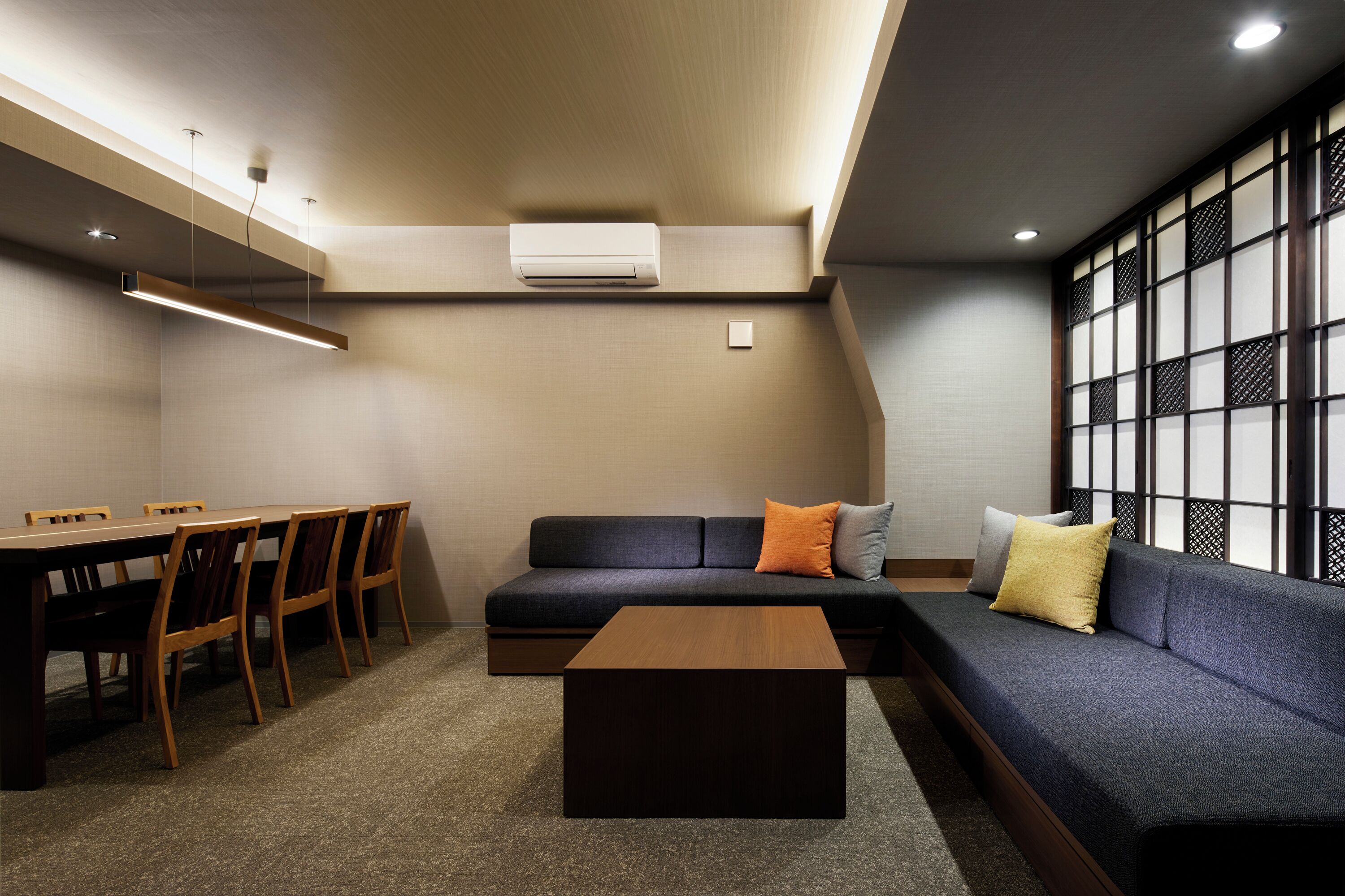 A modern living room with a sofa, a dining table with chairs, a coffee table, and a large window with a view.