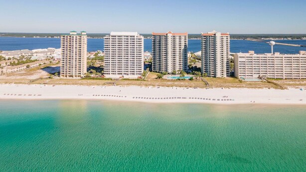 Ein Hotelkomplex an der Küste mit mehreren Hochhäusern, einem Strand und klarem türkisblauem Wasser.
