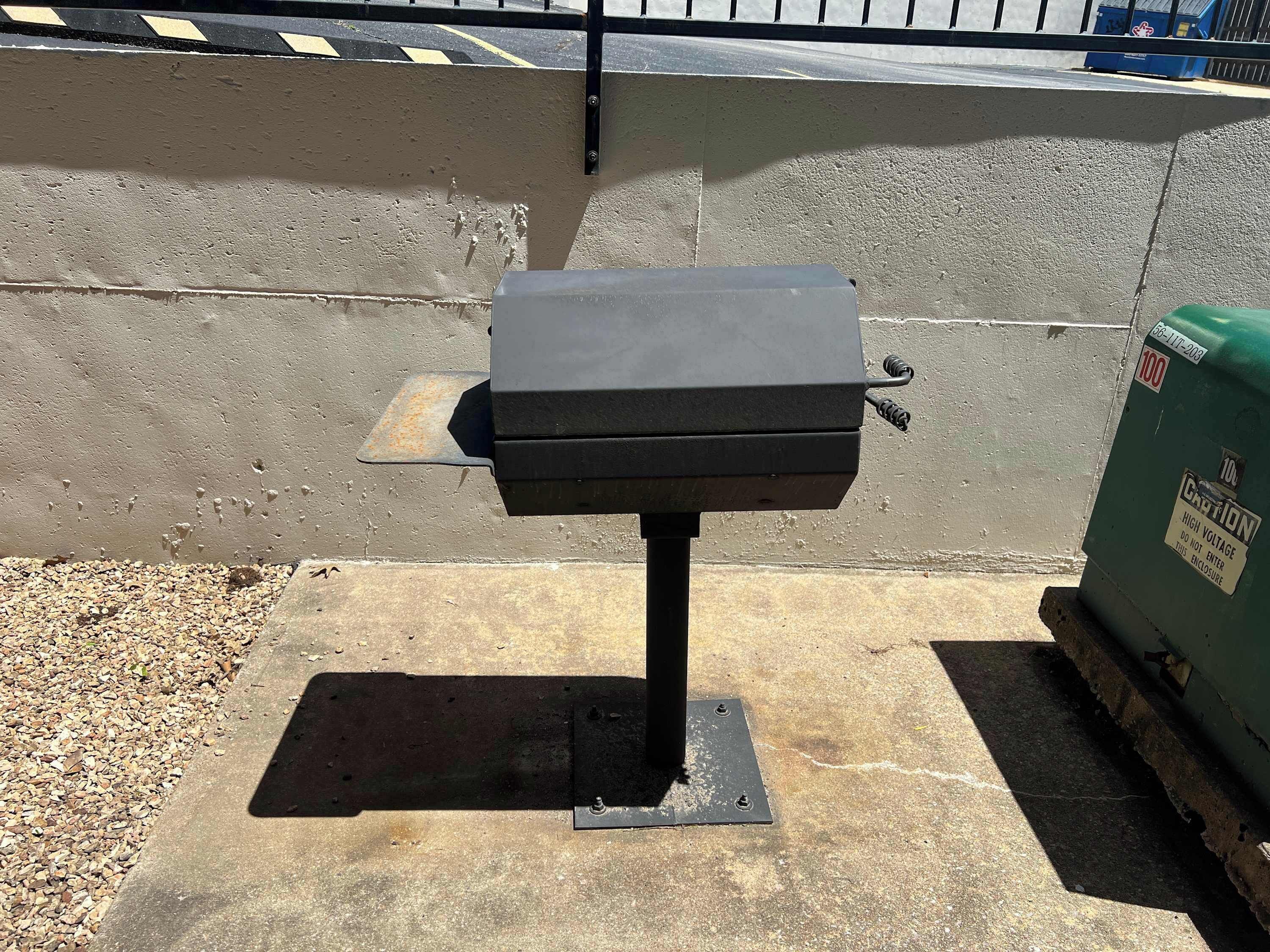 Een draagbare barbecue op een betonnen oppervlak, bevestigd aan een metalen standaard.