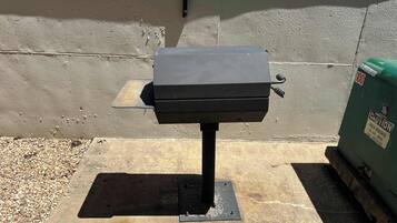 Een draagbare barbecue op een betonnen oppervlak, bevestigd aan een metalen standaard.