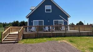 A two-story blue house with a wooden deck and a staircase leading to the entrance. - Newly Built Ocean View Cottage, Minutes To Thunder Cove Beach (Kensington)