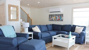 A living room with a blue sofa set, a white coffee table, and a staircase. - Newly Built Ocean View Cottage, Minutes To Thunder Cove Beach (Kensington)