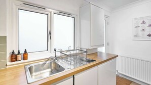 A modern kitchen with a stainless steel sink, wooden countertop, white cabinets, and a window with a view.