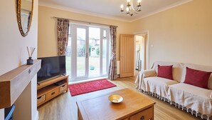 A living room with a TV, sofa, coffee table, and a sliding glass door leading to a garden. - Host & Stay | Wardman Crescent (Redcar)