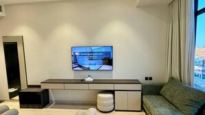 A modern hotel room with a bed, a sofa, a TV mounted on the wall, and a window with curtains. - Jadeel Hotel (Al Khobar)