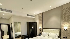 A modern hotel room with a large bed, a seating area, a wardrobe, and a bathroom visible through an open door. - Jadeel Hotel (Al Khobar)
