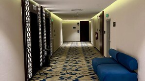A hotel hallway with patterned carpet, a blue sofa, and a row of doors. - Jadeel Hotel (Al Khobar)