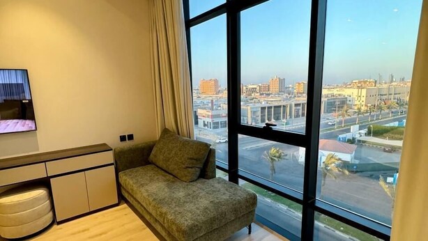 A modern living room with a large window, a sofa, a TV, and a small cabinet. - Jadeel Hotel (Al Khobar)