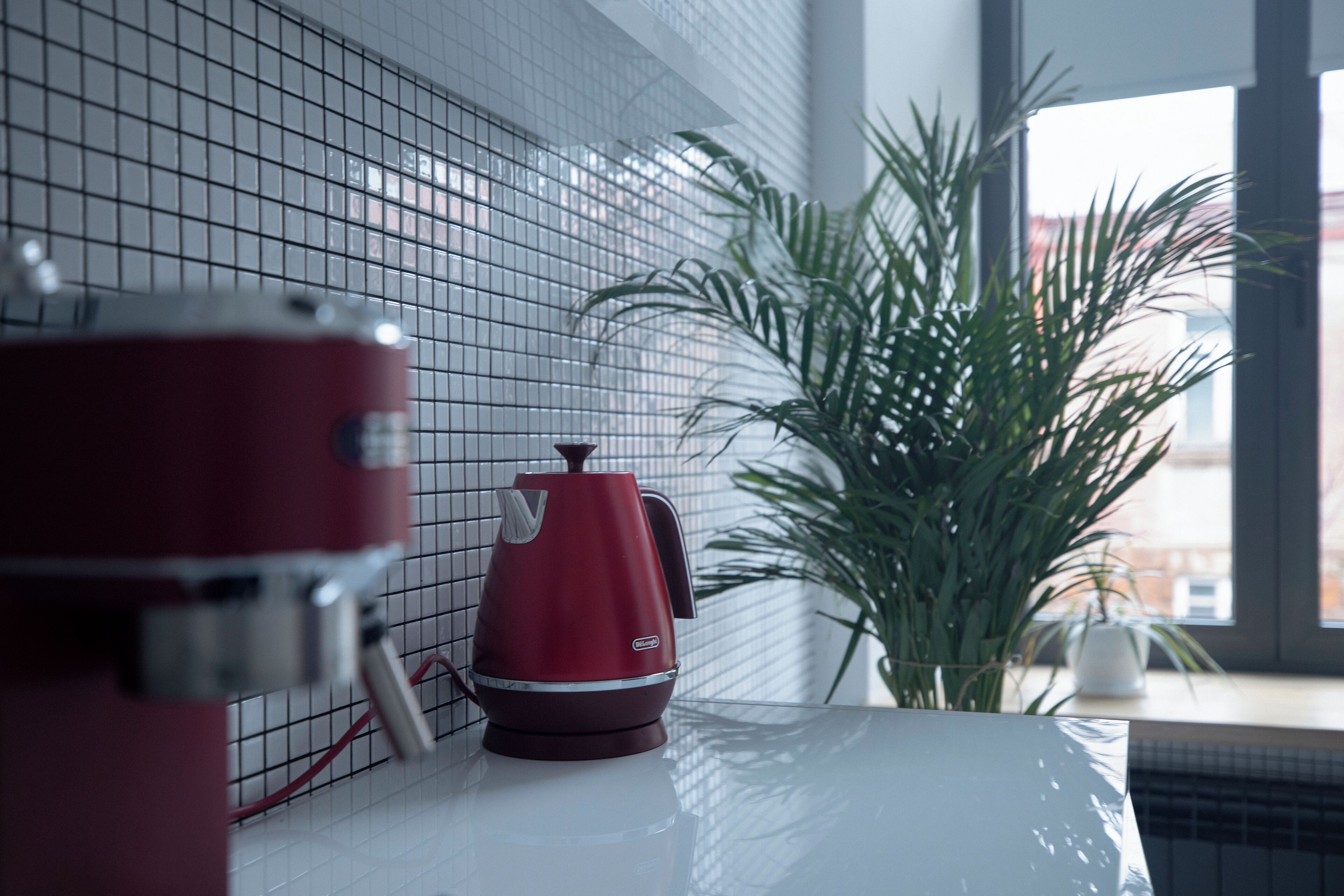 Una encimera de cocina con un hervidor rojo, una encimera blanca y una planta en maceta.