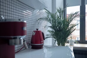 Una encimera de cocina con un hervidor rojo, una encimera blanca y una planta en maceta.