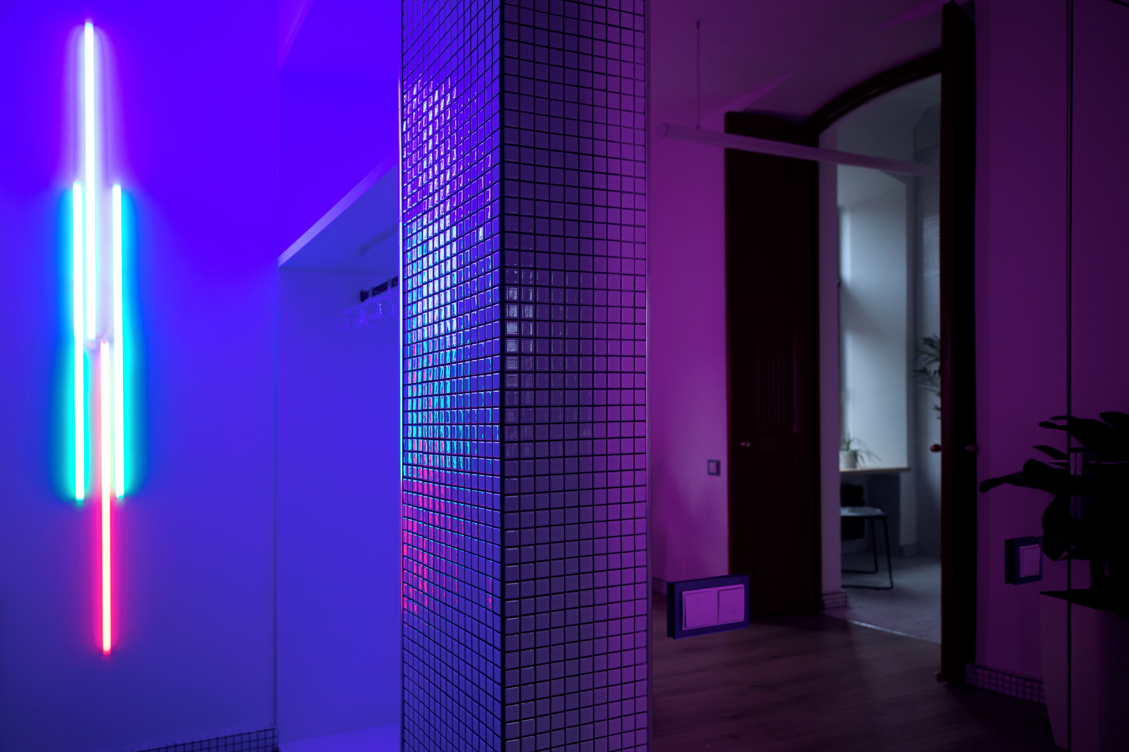 A modern interior with a vertical light installation, a tiled wall, and a doorway leading to another room.