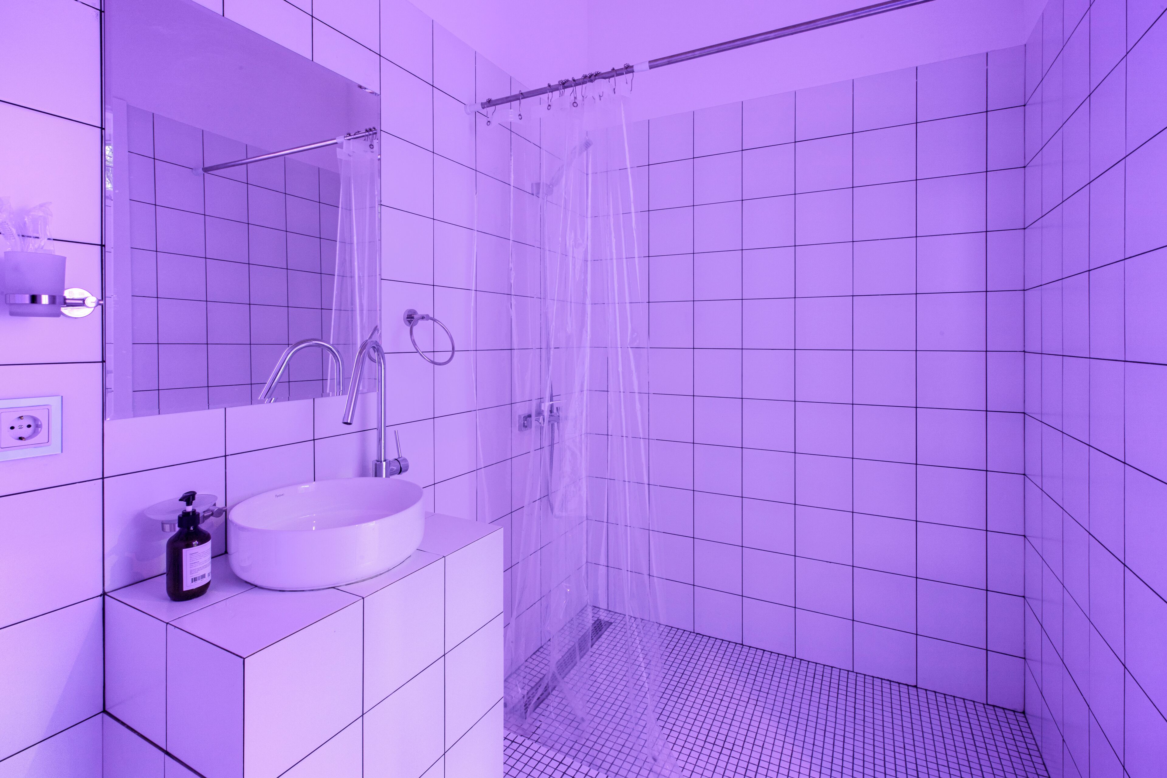 A bathroom with white tiles, a sink, a mirror, and a shower curtain.