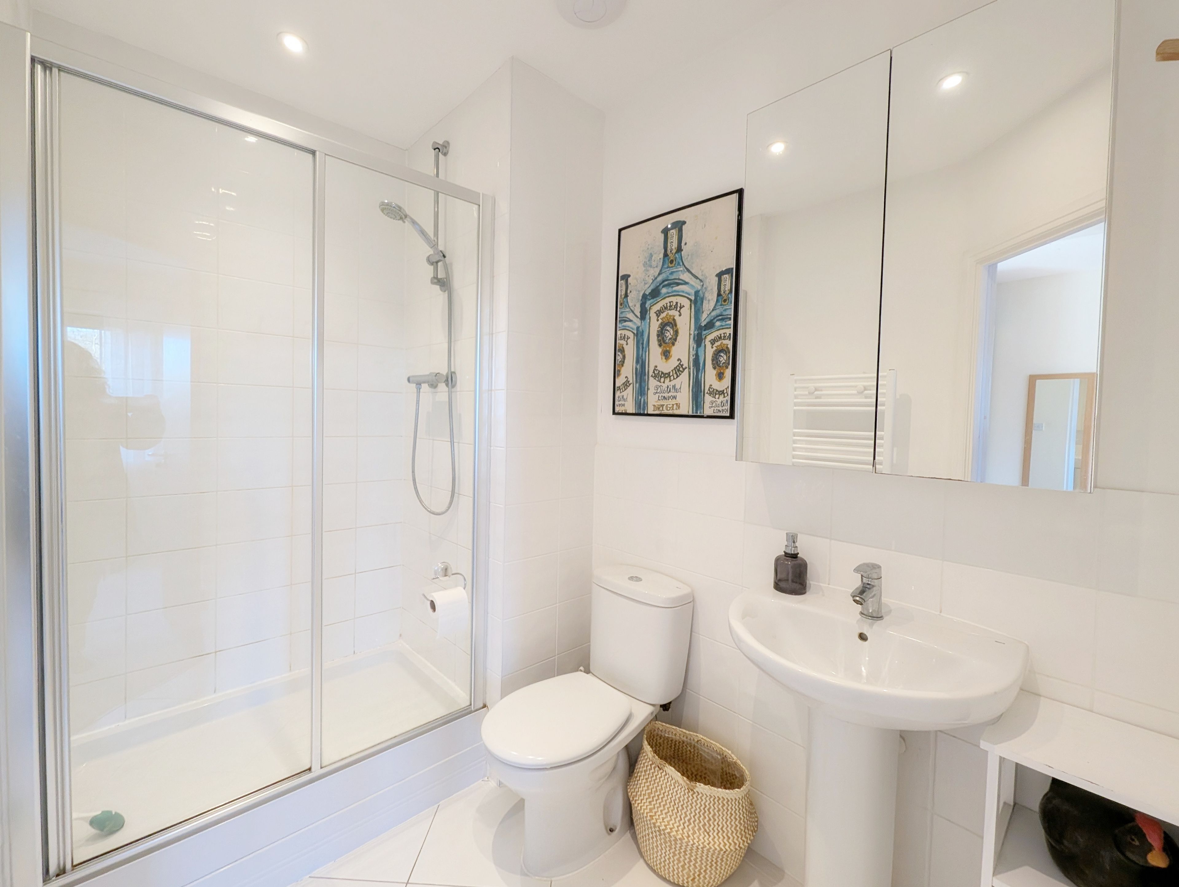 A modern bathroom with a glass-enclosed shower, a white toilet, a sink, and a framed artwork on the wall.