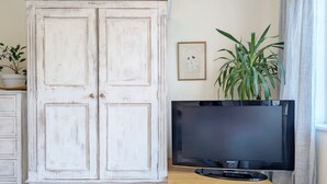A room with a white cabinet, a television on a wooden stand, a plant, and a framed picture on the wall.