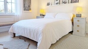 A bedroom with a large bed, two bedside tables with lamps, a radiator, a window with curtains, and a wall with framed pictures.
