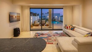 A modern living room with a sofa, a dining table, and a view of a pool through glass doors.