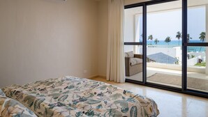 A bedroom with a bed, a window with a view of the beach, and a sliding glass door.